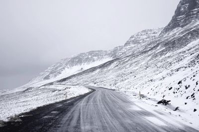 Country road amidst snowcapped landscape against sky