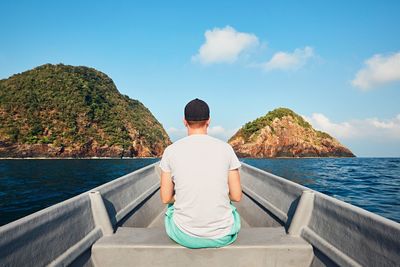 Rear view of man sitting in boat on sea against sky