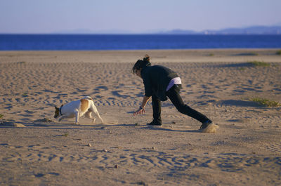 Woman playing with dog at beach against sky