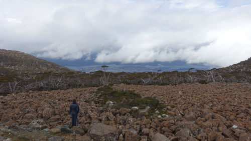 Rear view of woman standing on rocks against cloudy sky