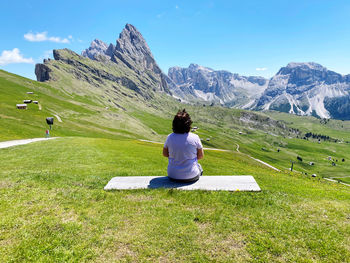 Rear view of woman sitting on grass against mountain