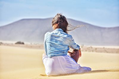 Rear view of woman sitting in desert during sunny day