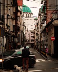 Rear view of man walking on street amidst buildings in city