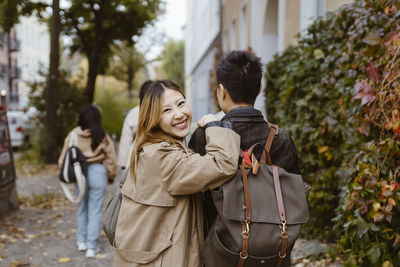 Portrait of happy woman looking over shoulder while walking with male friend on sidewalk