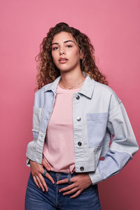 Portrait of teenage girl standing against pink background