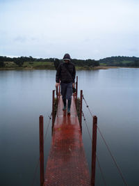 Full length of man in hooded jacket walking on pier over lake