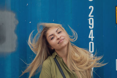 Portrait of young woman tossing hair against blue wall