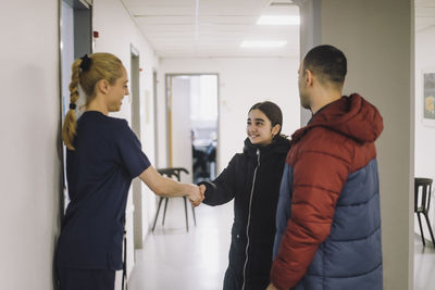 Smiling girl doing handshake with nurse standing in hospital corridor