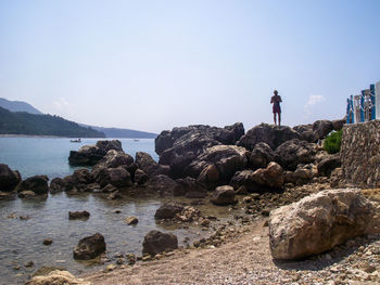 Man standing on rocks by sea against clear sky