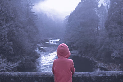 Rear view of boy standing against river and trees