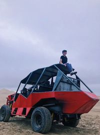 Young woman sitting on vehicle against sky