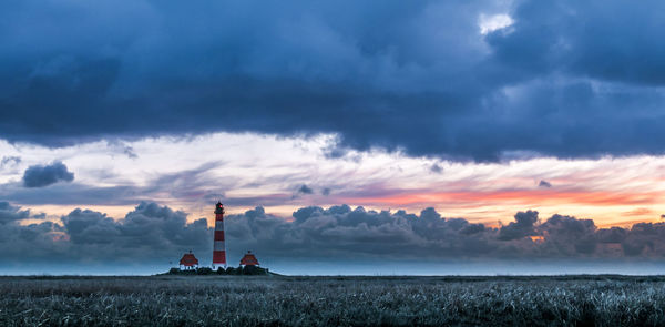 People on field by sea against sky during sunset