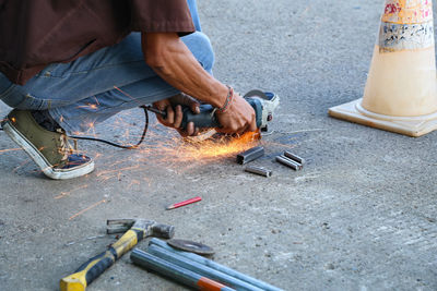 Low section of man cutting metal with electric saw on road