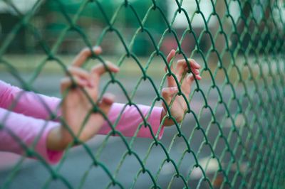 Cropped hands of woman on chainlink fence