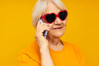Young woman wearing sunglasses against yellow background