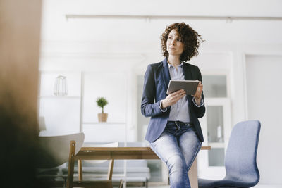 Businesswoman in office sitting on desk, using digital tablet