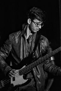 Young man playing guitar against black background