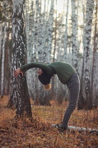 Woman exercising by tree trunk in forest during winter