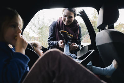 Smiling mother helping daughter to wear boot in car