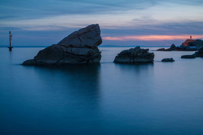Rocks in sea against sky during sunset