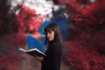 Young woman looking away while standing against trees during autumn