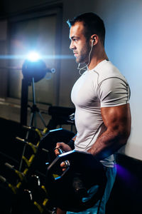 Side view of man lifting dumbbell while listening music in gym