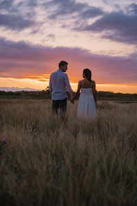 Rear view of woman walking on field against sky during sunset