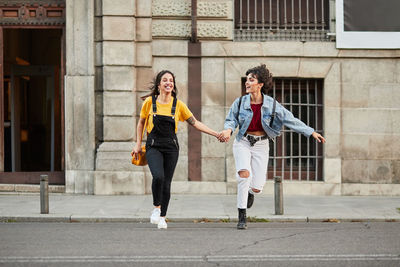 Full length of women holding hands running on road against building