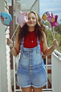 Portrait of smiling young woman holding balloons while standing in balcony