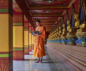 Monk reading by buddha in temple