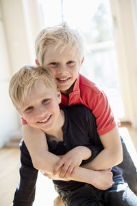 Portrait of boy embracing brother from behind in house