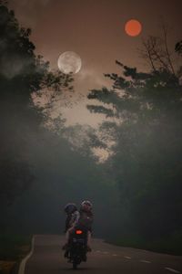 People riding motorcycle against sky at night