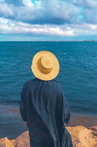 Rear view of woman wearing hat standing against sea and sky
