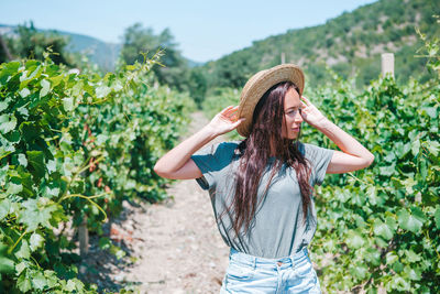 Young woman wearing hat standing against plants
