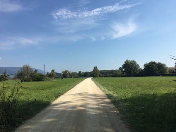 Empty road amidst field against sky