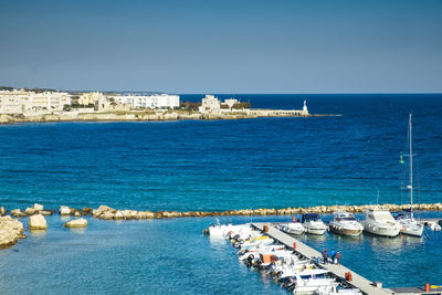 High angle view of motorboats moored at harbor against blue sky