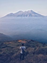 Rear view of man standing on mountain against sky