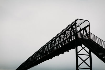 Silhouette of iron bridge against grey sky.