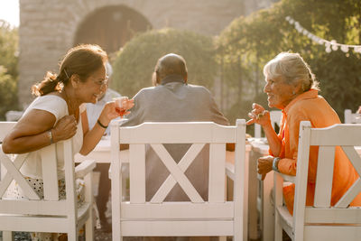 Smiling retired senior women talking behind man while sitting at back yard