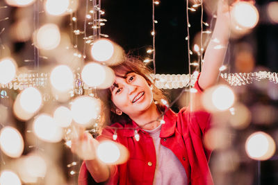 Portrait of smiling young woman with illuminated string lights at night