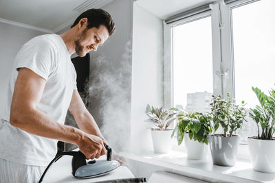 Side view of man ironing clothes at home