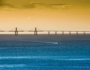 Silhouette bridge over sea against sky during sunset