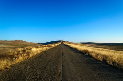 Road amidst field against clear blue sky