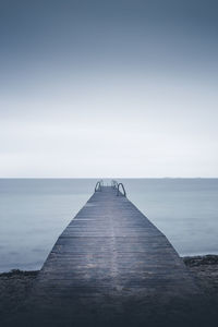 Jetty leading towards sea against clear sky