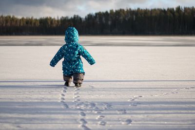 Full length rear view of baby boy wearing warm clothing while walking on snow