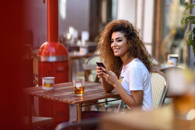 Smiling young woman using smart phone while sitting at outdoors cafe