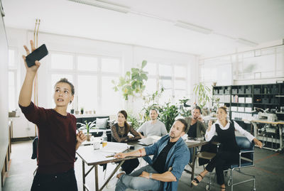 Businesswoman explaining coworker over whiteboard during meeting in creative office