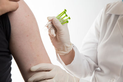 Midsection of doctor injecting syringes on patient arm against white background