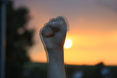 Close-up of hand against orange sky during sunset