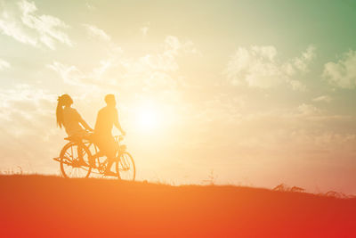 Silhouette man riding bicycle on field against sky during sunset